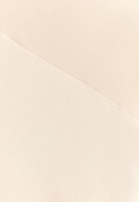 Světle béžová látka s hladkým, strukturovaným povrchem. Diagonální šev vytváří dvě odlišné sekce, což zdůrazňuje skládací kvalitu materiálu.