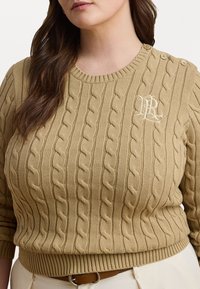 Strikkegenser i beige med ribbede mansjetter og kant. Har kabelstrikkemønster, rund halslinning og to-knaps detalj på skulderen. Monogramlogo.