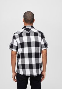 Kortebloes met een zwart-wit ruitpatroon, voorzien van een klassieke tartanprint, knoopsluiting bij de kraag en een relaxed fit. Gemaakt van katoen.