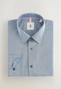 Skjorte med knapper i blåt geometrisk mønster, kontrasterende kraveforing og lomme detalje. Har lys blå knapper og en struktureret krave.