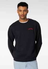 Svart hettegenser laget av bomullsblanding, med ribbestrikket rund hals, lange ermer, og rødt brodert tekst "HENRY CHOICE" på brystet.