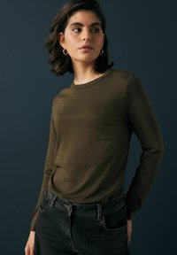 Olivenfarbendes Langarmshirt aus weichem Stoff mit Rundhalsausschnitt. Kombiniert mit hoch taillierten schwarzen Jeans mit klassischem Fünf-Taschen-Design.
