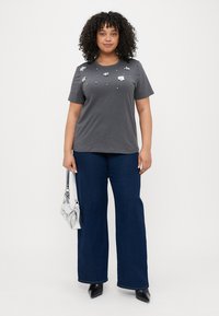 Grå bomull t-skjorte med blomsterdekorasjoner og perler, sammen med blå vide jeans og svarte spisse hæler. Sølv veske.