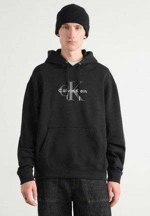 Zwarte katoenen hoodie met een voorste kangaroo pocket, voorzien van een bedrukte Calvin Klein-logo in grijs en verstelbare koordjes bij de capuchon.
