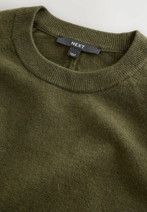 Olivengrüner Strickpullover mit ribbeligem Rundhalsausschnitt. Aus weichem Material gefertigt, mit einem schlichten Design und subtiler Textur. Das Etikett trägt die Aufschrift "NEXT."