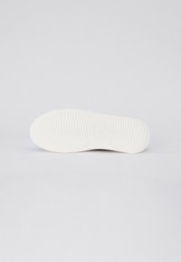 Fehér sneaker talp vízszintes bordázott mintázattal, lekerekített formával és lapos aljjal. Az anyag gumihoz hasonlónak tűnik. Látható márkajelzés vagy díszítés nélkül.