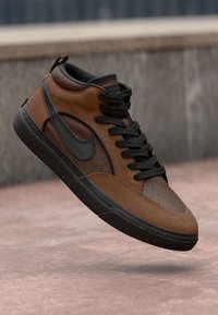 Braune und schwarze High-Top-Sneaker mit schwarzen Schnürsenkeln und Nike-Swoosh-Logo, schwebend über einer Betontoberfläche.