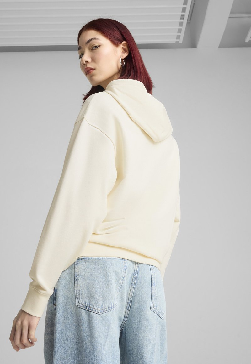 Sudadera color crema con capucha ajustable, corte relajado y textura suave, combinada con unos vaqueros de denim de tiro alto en azul claro.