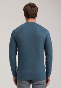 Maglione texture blu scuro con scollatura rotonda, maniche lunghe e polsini e orlo a costine. Presenta un sottile motivo a diamante.