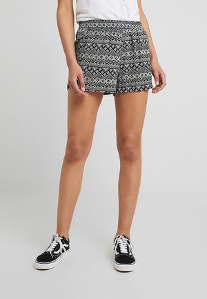Shorts à motifs noir et blanc avec une taille élastique, présentant un design géométrique, fabriqués en tissu léger. Portés avec des baskets noires.