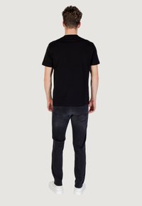 Maglietta nera a maniche corte abbinata a jeans scuri, vista da dietro. I jeans presentano tasche posteriori con dettagli discreti. Sneakers bianche completano il look.