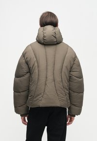 Casaco puffer isolado verde com gola alta e costura destacada. Apresenta mangas exageradas e um corte descontraído.