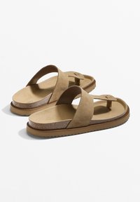 Bruna mockasinsandaler med V-formade remmar, texturerad fotbädd och en flexibel gummisula, med en subtil detalj nära tån.