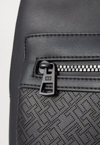 Black faux leather bag featuring a textured bottom with geometric cut-out pattern. Includes a metal zipper with a rectangular pull tab.