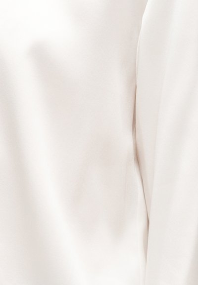 Κοντινό πλάνο λείου, εκρού υφάσματος με λεπτές ρυτίδες και απαλή πτυχή στη δεξιά πλευρά.