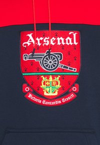 Hoodie med röd övre del och marinblå nedre del. Har en broderad Arsenal-logotyp med kanon, gröna detaljer och text nedan.