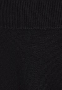 Maglione nero in maglia con una texture a coste sul colletto e un corpo morbido e liscio. Nessun motivo o dettaglio in metallo visibile.
