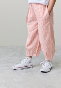 Pantaloni ampi a righe rosa e bianche con tasche laterali, abbinati a sneakers alte bianche con accenti blu e rossi.