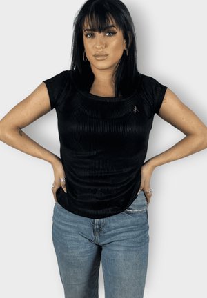 Camiseta negra de canalé con escote redondeado y mangas cortas, que presenta un sutil acento de logo, combinada con jeans de color azul claro.