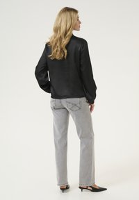 Blusa de satén negro de manga larga combinada con jeans rectos gris claro y tacones negros tipo slingback. Textura suave con un ajuste relajado.