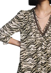 Tiermotiv-Bluse in Beige und Schwarz, mit tiefem V-Ausschnitt, gerafften Details und Drei-Viertel-Ärmeln mit umgeschlagenen Bündchen.