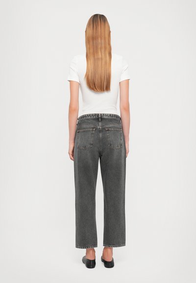 Jeans a vita alta e gamba larga in denim grigio scuro con orli sfrangiati e tasche posteriori, abbinati a una t-shirt bianca aderente.