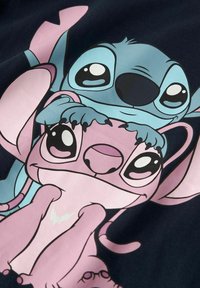 T-shirt graphique avec deux personnages de bande dessinée : une figure rose avec de grands yeux et une figure bleue avec un nez proéminent, sur un fond sombre.