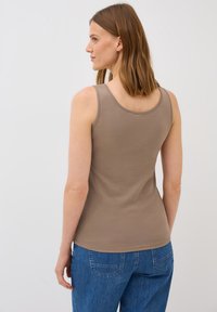 Top sin mangas de color marrón, hecho de una tela suave y acanalada. Presenta un escote en forma de U y una silueta ajustada, combinado con jeans azules.