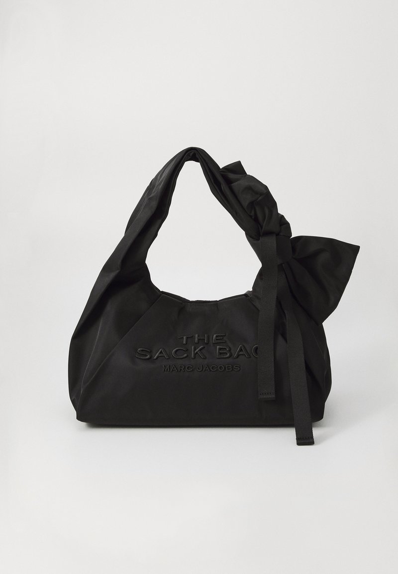 Saco de tecido preto com uma alça atada e um grande laço. A parte da frente apresenta texto em relevo que diz "THE SACK BAG MARC JACOBS."
