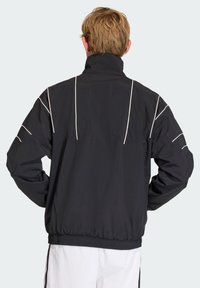 Black windbreaker jacket viewed from the back, featuring white piping details, elastic waistband, and a high collar.