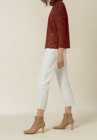 Top di pizzo rosso con maniche lunghe, pantaloni bianchi a cappuccio e stivaletti beige con tacco a blocco e zip laterale.