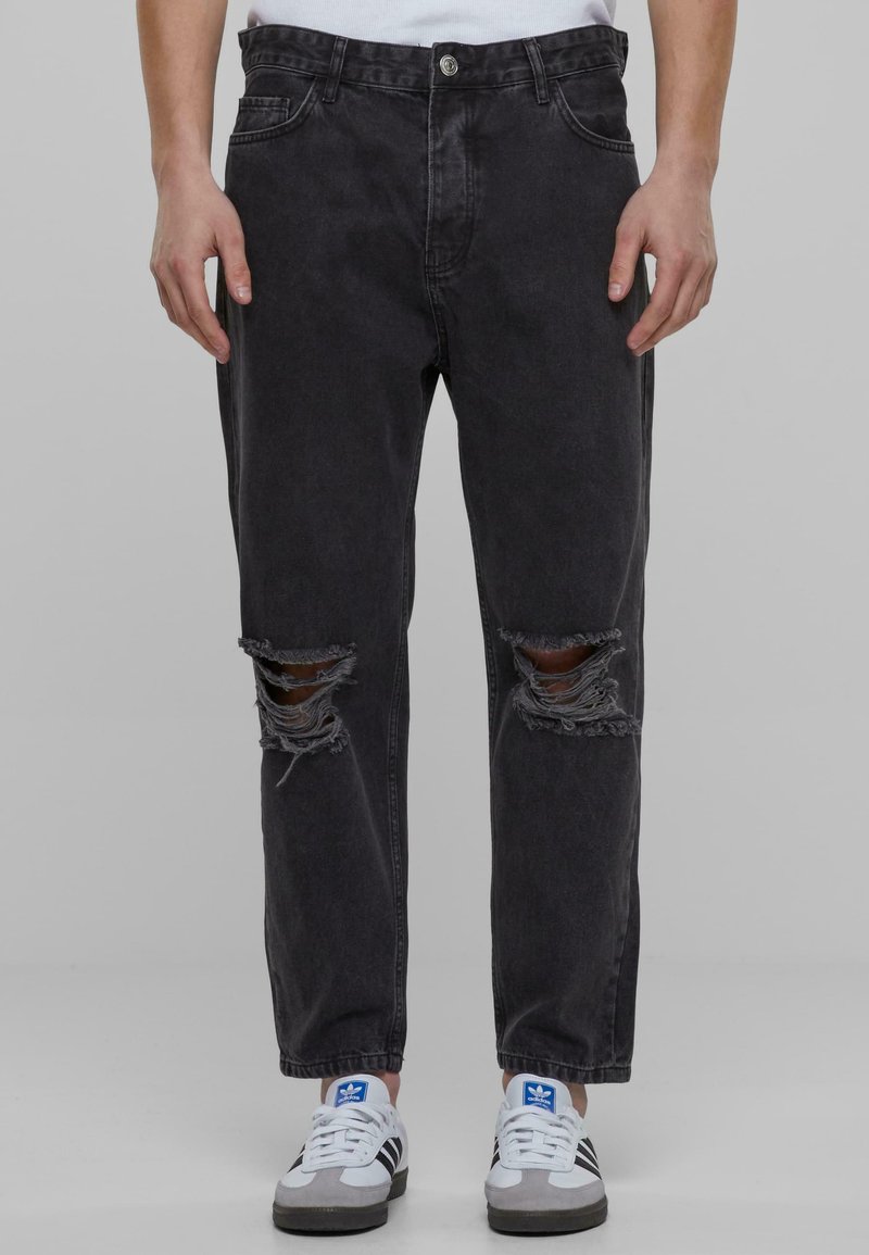 Črne denim hlače z ohlapnim krojem, z raztrganinami na kolenih in rahlim zbledeljem. Kovinski gumb in zasnova s petimi žepi.