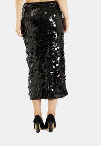 Falda de lentejuelas negras con un diseño ajustado, corte a la altura de la rodilla y textura suave. Combinada con zapatos de tacón alto negros.