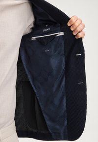 Giacca slim-fit blu navy con un'esterno testurizzato e un interno a motivo liscio, dotata di tasche interne e dell'etichetta JOOP! visibile.
