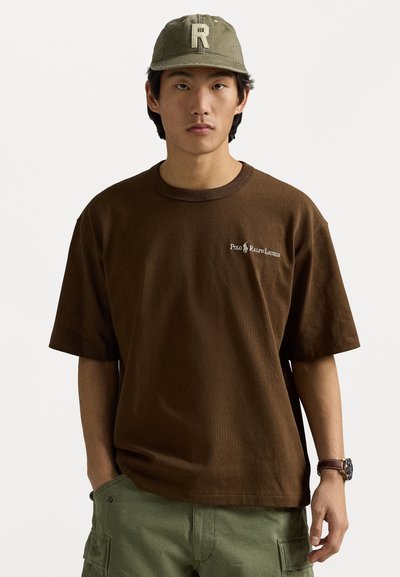 Tricou ribbed maro, cu mânecă scurtă și decolteu rotund, cu logo pe pieptul stâng; asortat cu pantaloni scurți cargo verzi și o șapcă verde deschis.