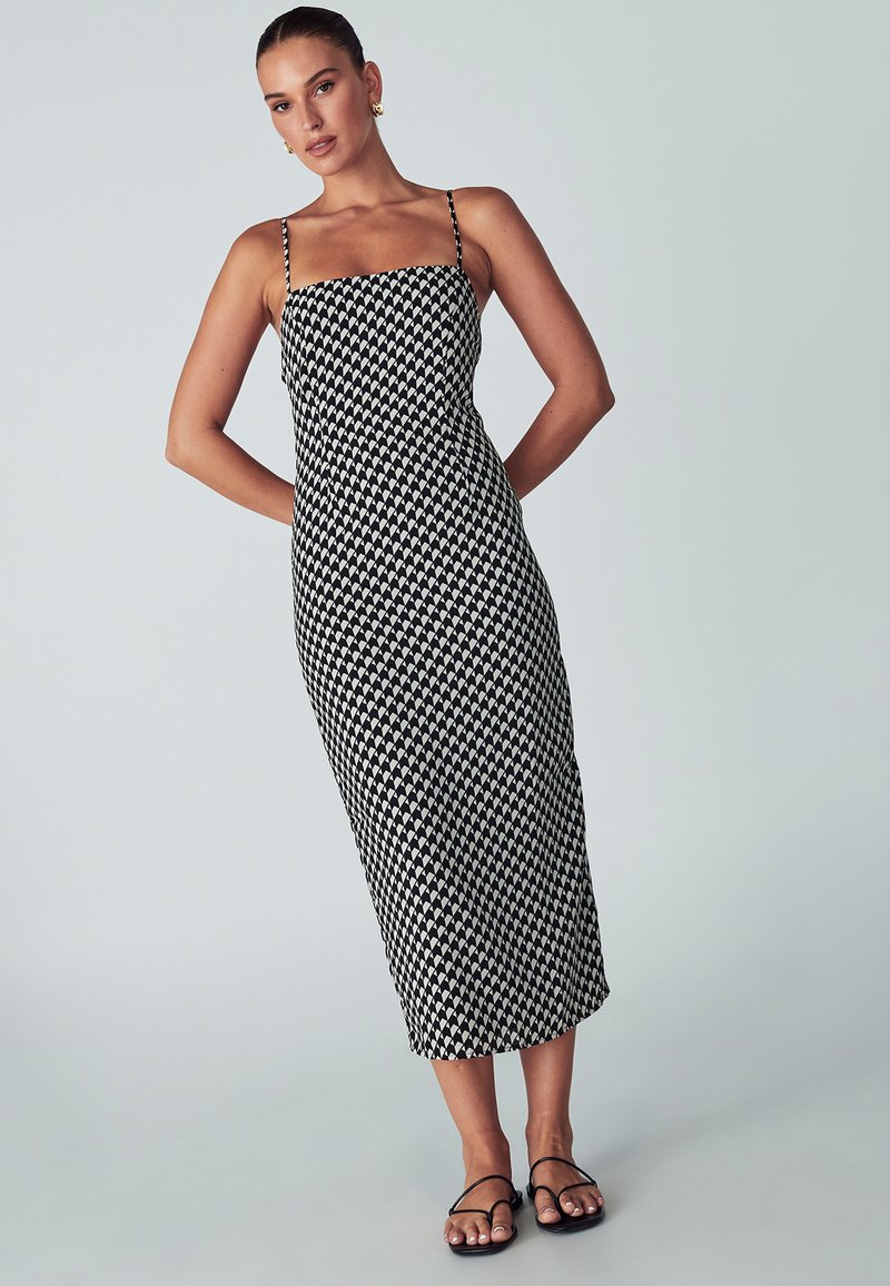 Musta-valkoinen kuviollinen midi-mekko, jossa on ohuet hihnat, vartalonmyötäinen yläosa ja suora siluetti, esillä vaaleaa taustaa vasten.