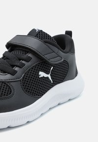 Chaussure de sport noire dotée de panneaux en mesh, d'un col rembourré et d'une semelle en caoutchouc blanche. Comprend un laçage et une sangle Velcro. Accent de logo blanc.