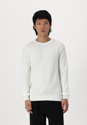 Maglione bianco a coste con scollo rotondo e maniche lunghe, caratterizzato da un knitting testurizzato. La vestibilità è leggermente ampia, abbinato a pantaloni neri.