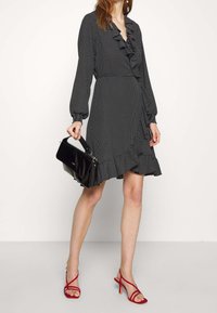 Vestido negro con lunares blancos, con escote con volantes y mangas con puños, que presenta un dobladillo acampanado. Combinado con un bolso negro y sandalias rojas con tiras.