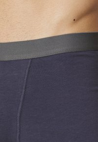 Boxeri cu talie joasă de culoare bleumarin, cu un elastic gri, având o textură netedă și un design ajustat, evidențiind detaliile cusăturii la cusătură.