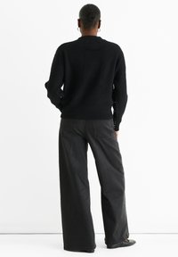 Black knitted sweater with ribbed texture, featuring button accents on sleeves. Paired with wide-leg dark jeans and black shoes.