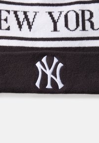 Căciulă tricotată neagră cu dungi orizontale albe. Prezintă textul "NEW YORK" în negru și un logo brodat alb "NY". Textură moale.