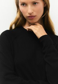 Zwarte sweatshirt met een ronde hals, lange mouwen en een zachte textuur; getoond op een model met een neutrale achtergrond.