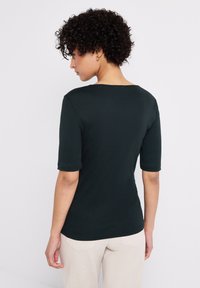 Mörkgrön t-shirt med kort ärm och rundad halsringning i slim fit, tillverkad av mjukt tyg, i kombination med ljusbeige byxor.