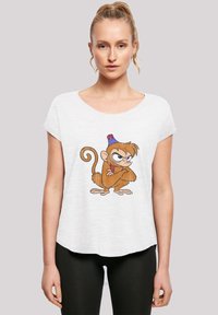 Hvit T-skjorte med kort erm som har et tegneserieape-trykk med blå hatt og brun pels, vist over svarte leggings.