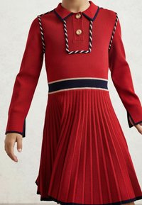 Vestito rosso lavorato a maglia con scollatura colletto, due bottoni prominenti, gonna a pieghe e accenti blu navy e crema su polsini e vita.