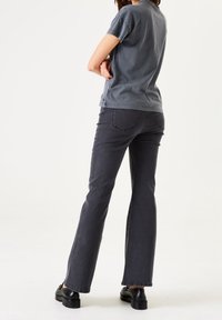 Grå bomullströja med korta ärmar som matchas med mörkgrå flarejeans. Båda har en avslappnad passform och en mjuk textur. Svarta skor fulländar looken.