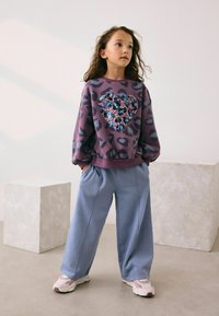 Lilla sweatshirt med leopardmønster og en palietteret hjerte, parret med lyseblå vide bukser og lyserøde sneakers.