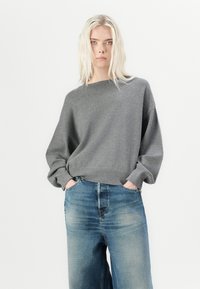 Grijze gebreide trui met een brede halslijn en een losse pasvorm, gecombineerd met blauwe denim spijkerbroeken. De trui heeft ribgebreide manchetten en een ribgebreid boord.