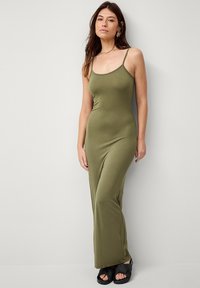 Olijfgroene, aansluitende maxidress met dunne bandjes, gemaakt van gladde stof. Gecombineerd met zwarte, strap sandals. Eenvoudig, strak ontwerp.
